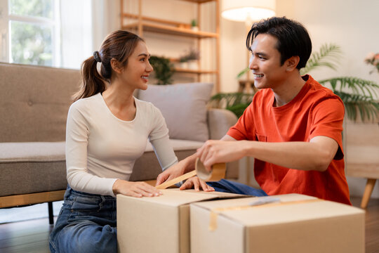 Asian adult couple happily packing moving boxes new home together cozy living room preparing for a fresh start relocation