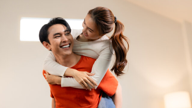 Asian couple laughing piggyback ride home living room playful joyful relationship bond intimate moment togetherness happiness