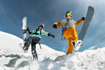 Two happy young snowboarders are having fun and jumps with snowboards from snowdrift. Winter vacations at ski resort concept