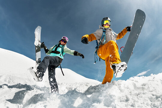 Two happy young snowboarders are having fun and jumps with snowboards from snowdrift. Winter vacations at ski resort concept