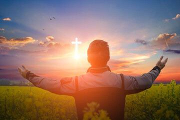 Christian man worshiping the christian cross in the field at sunset