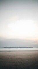 Minimalist landscape featuring a blurred beach foreground, a calm sea, a distant island, and a soft, hazy sky.