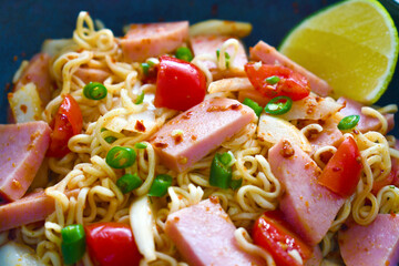 Spicy noodle salad with ham onion tomatoes chillies and lemon in a bowl. Asian food.