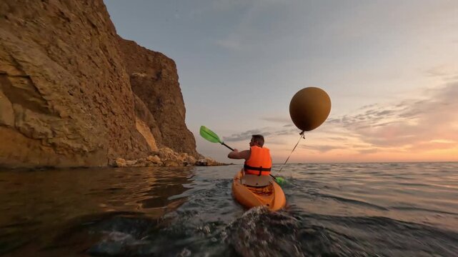 Kayak man sunset paddling along rugged cliff exploring calm sea at golden hour adventure - Powered by Adobe