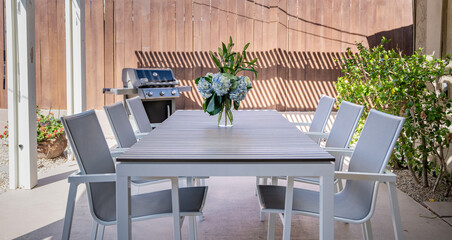 Outdoor patio table in a backyard, chairs, grill, and floral bouquet.