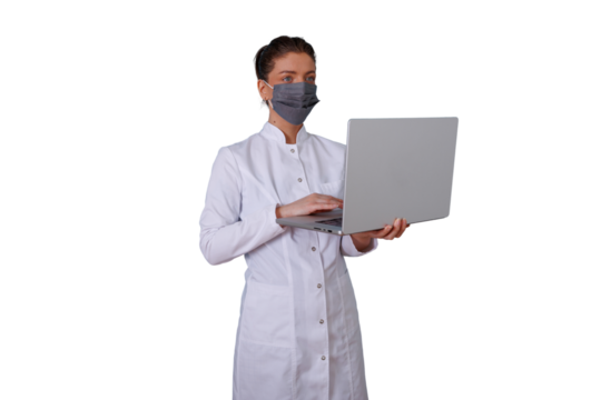 Female medical professional wearing face mask and lab coat, typing on laptop, working in healthcare technology
