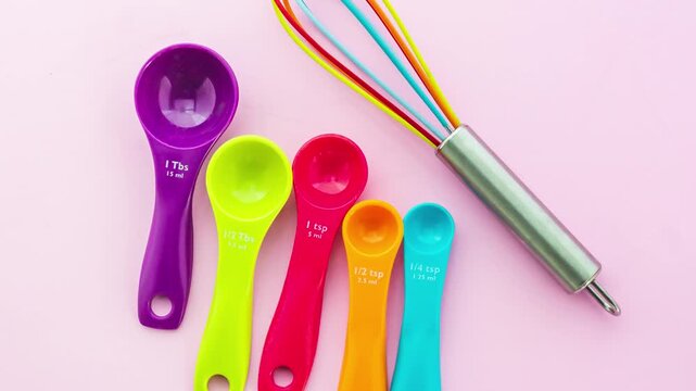 Colorful Measuring Spoons Set and Silicone Whisk Rotating on Pink Background