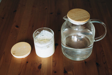 Glass jar with sourdough starter and water pitcher on wooden table  