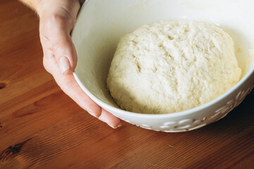 Hand holding bowl of kneaded sourdough dough on wooden table  