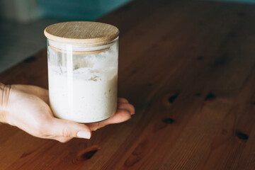 Hand holding jar of active sourdough starter on wooden table  
