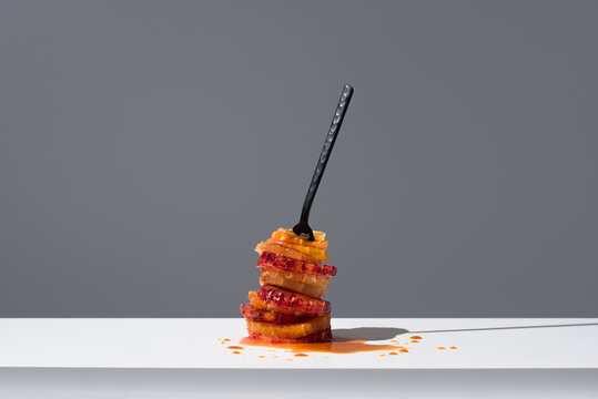 Rodajas de frutas c&iacute;tricas peladas con caramelo l&iacute;quido pinchadas con un tenedor sobre una mesa blanca y fondo gris oscuro