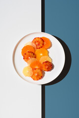 Surtido de rodajas de cítricos peladas en un plato blanco sobre fondo azul y blanco. Vista...