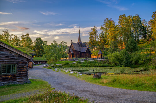 Historic Garmo Stave Church, also known as Garmo stavkirke, surrounded by traditional log buildings and forested sunset landscape in Lillehammer, Norway.