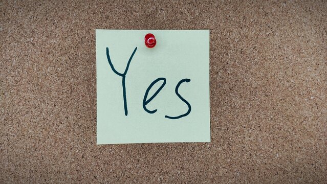 Sticky note with handwritten word YES on cork board – motivation and positive mindset concept