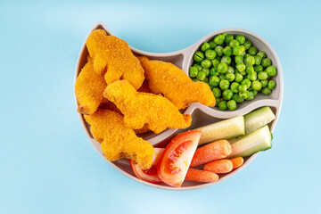 Tasty kids food, dinosaur shaped chicken nuggets. Plate with dino nuggets and sauce and vegetables, healthy and fun air fried dino nuggets