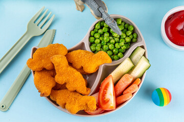 Tasty kids food, dinosaur shaped chicken nuggets. Plate with dino nuggets and sauce and vegetables, healthy and fun air fried dino nuggets