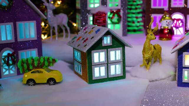 An orange car with a Christmas tree on the roof drives past the small houses of a large Christmas village