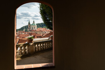 Prague, Czech Republic – August 6, 2025: View of St Nicholas Church in Malá Strana framed by a garden arch, with red rooftops and forested Petřín Hill in Prague, Czech Republic, on a summer afternoon