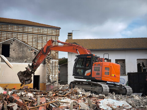 Escavadora hidráulica em ação na demolição de um edifício sob céu nublado, em meio a um grande monte de entulho e detritos ao redor da obra