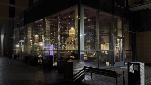 Restaurant outdoors with warm light shining through glass windows at night, cozy illuminated