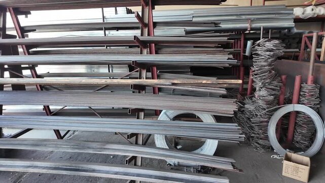 A metal storage yard for construction &mdash; chain-link mesh (rabitz) and steel rebar stacks on site, industrial equipment in factory.
