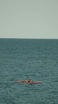 Woman, ocean, relaxing, a woman tans on a paddleboard in the vast open sea on a sunny day. Vertical video