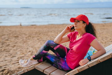 Relaxed woman talks on the phone while reclined on a beach bench, enjoying the peacefulness of the seaside.