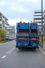 Naklejka premium Blue waste collection truck parked on a residential street with modern apartment buildings in the background.
