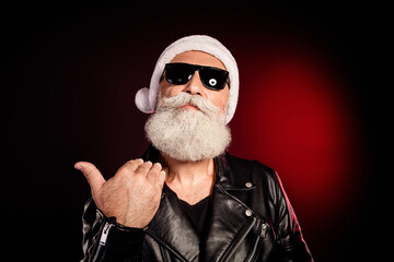 Santa rocker in leather jacket with white beard and hat gives thumbs up against dark red background for festive christmas theme