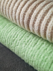 close-up stack of rolled cozy fabrics: beige ribbed knit, pale green knit and dark gray texture