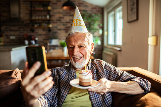 Senior man smiling on video call with birthday cake at home - Powered by Adobe