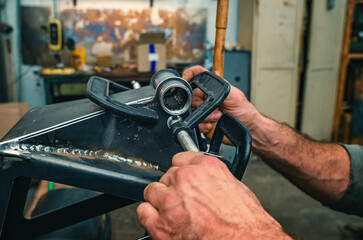 Fototapeta premium Male hands tighten metal parts together with clamp. Clamp has threaded screw. Industrial workshop.