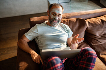 Mature man smiling on video call with face mask at home