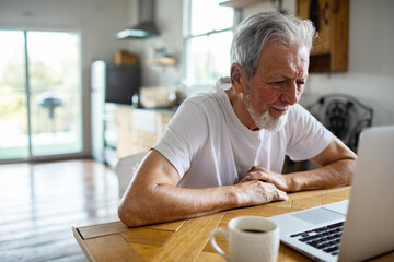 Senior man smiling while using laptop at home