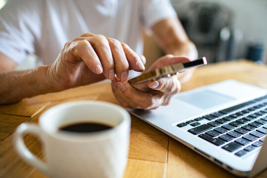 Senior adult focused using smartphone and laptop at home table
