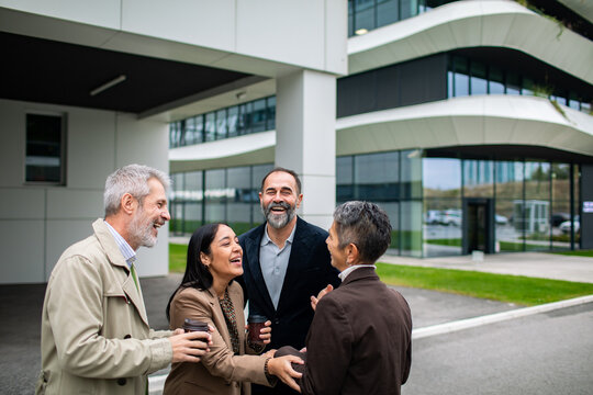 Adult colleagues laughing during coffee break outside modern office