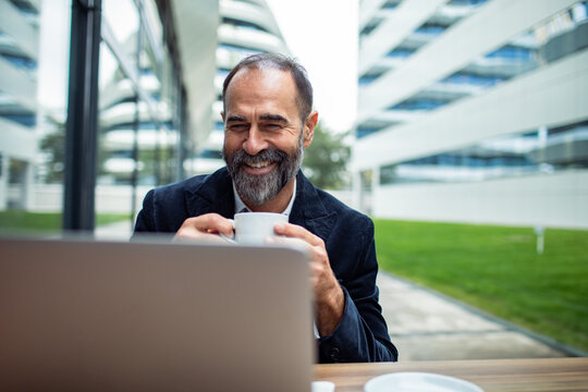 Mature man smiling over coffee while working on laptop at office courtyard