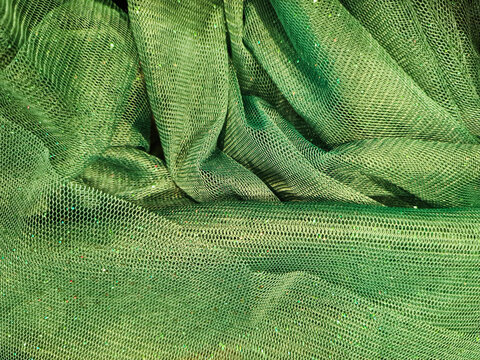 Background of metallic green tulle with glitter particles. Handmade green tulle with a subtle sheen and woven in a hexagonal pattern, for decoration, fashion purposes, or crafts material.