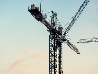 Crane silhouettes against pastel twilight sky with moon over construction site during evening