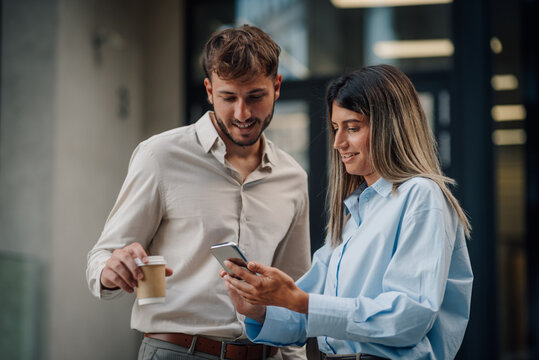 Business partners looking at smartphone and drinking coffee during a break outside the office