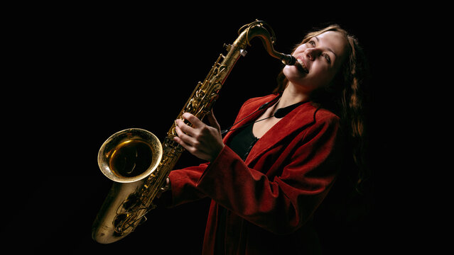 Woman in red jacket playing saxophone passionately on dark background. Concept of music posters, creative advertising, psychology of emotion, and motivational visual storytelling.