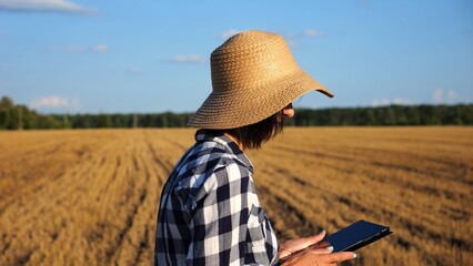 Adult farmer using digital tablet at wheat meadow on sunny day. Female agronomist monitoring harvest at barley field. Beautiful scenic landscape. Concept of agricultural business. Slow motion