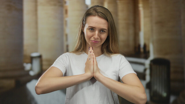 Woman praying with hopeful expression in historic old town street with columns and soft lighting.