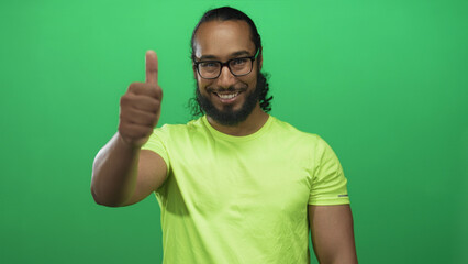 Man giving thumbs up with exposed hand and smiling in a green studio setting wearing neon tee and glasses; optimism.