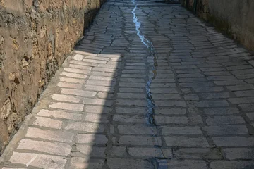 Selbstklebende Fototapeten Enge Straßen The water flows through the ancient narrow streets of the ancient city. Ancient quarters of the city of Derbent. Ancient sandstone houses. Narrow streets in an ancient city in the Caucasus.  © Eduard Belkin