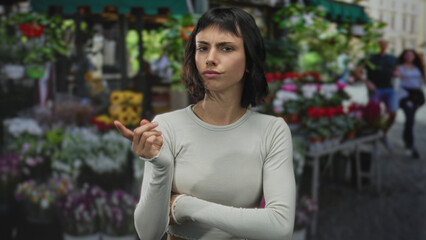Young hispanic woman lifts index finger amid vibrant flower bouquets at a street market;...