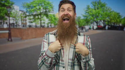 Man clenching fists in busy city street wearing plaid shirt and sporting long beard with intense...