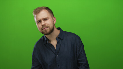 Man tilts head, chest exposed and wearing dark blue shirt in studio with bright green backdrop; thoughtful introspection.