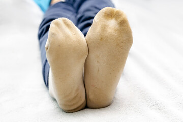Child feet in dirty stained white socks.Kid soiled contaminated socks while playing outdoors,on unwashed floor.Children clothes bleaching and washing troubles concept