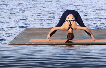 Young latin hispanic woman practicing Prasarita Padottanasana on a sandy beach by the ocean. Morning yoga for flexibility, balance, and inner peace in a serene coastal setting wide legged forward bend